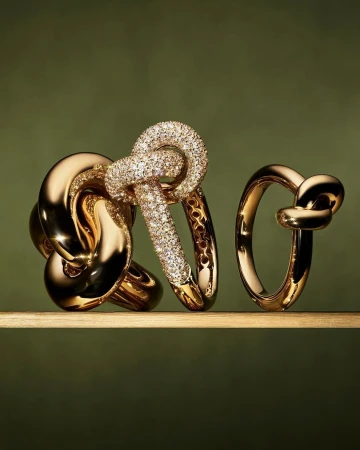 Close-up of three gold and diamond rings of varying sizes on a reflective surface against a green backdrop in a studio setting.