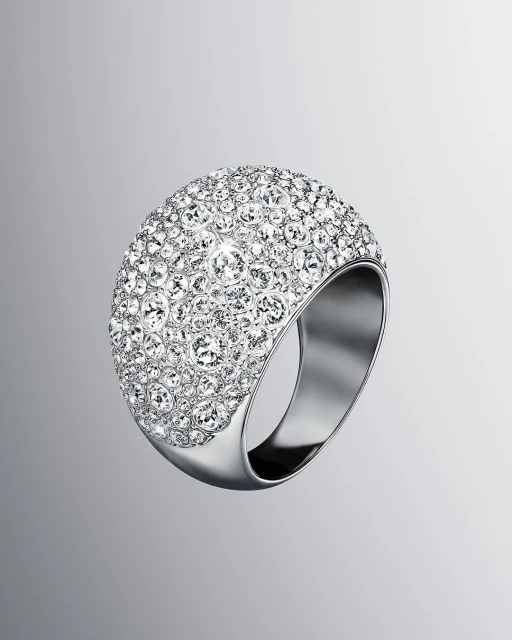 Close-up of a large, dome-shaped ring encrusted with clear crystals, set on a silver metal band against a gradient grey background.