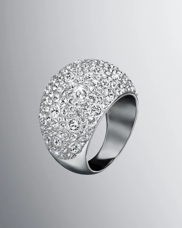 Close-up of a large, dome-shaped ring encrusted with clear crystals, set on a silver metal band against a gradient grey background.