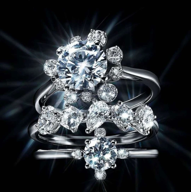 Three shimmering diamond rings are stacked against a black background, illuminated by bright light reflections on the jewelry.