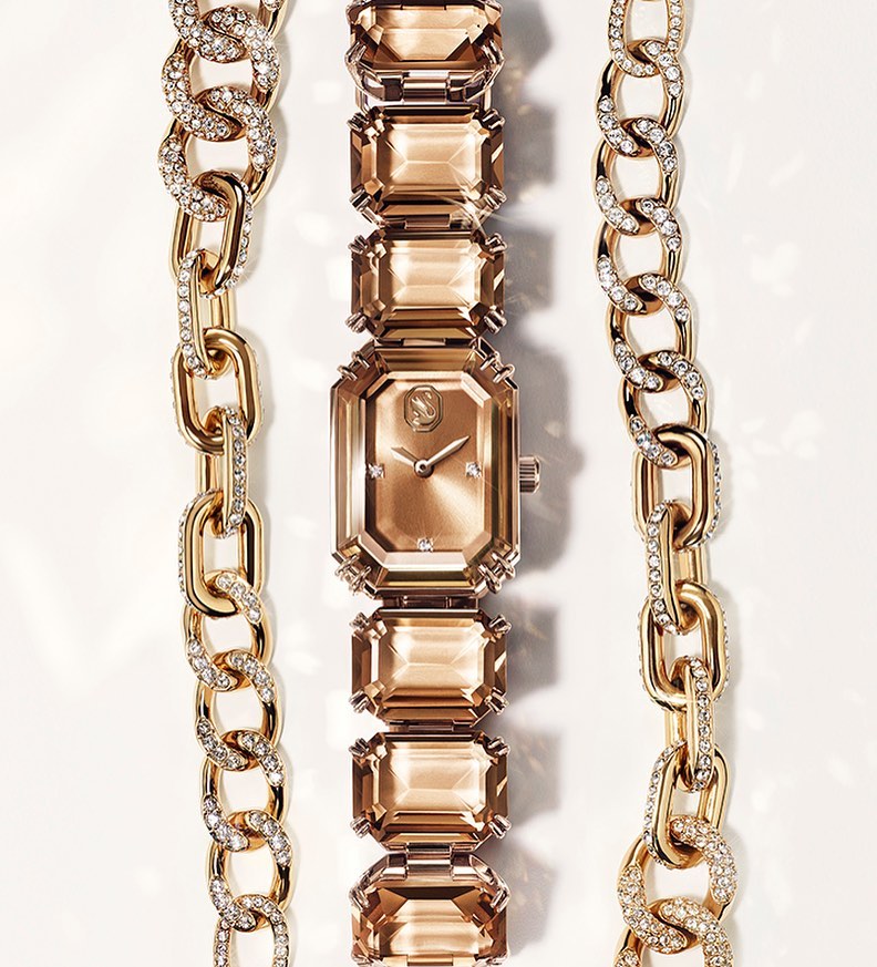 Elegant rose gold-tone watch with crystal-studded gold chains on a white surface, showcasing luxury jewelry design and timekeeping.