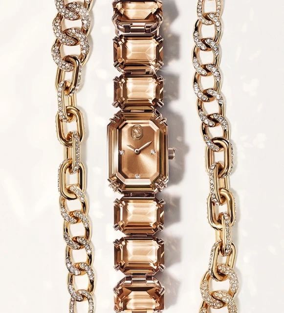 Elegant rose gold-tone watch with crystal-studded gold chains on a white surface, showcasing luxury jewelry design and timekeeping.