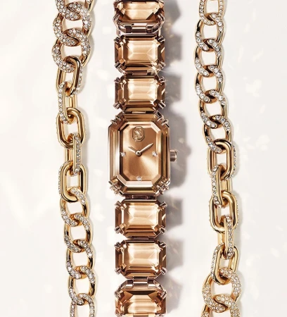 Elegant rose gold-tone watch with crystal-studded gold chains on a white surface, showcasing luxury jewelry design and timekeeping.