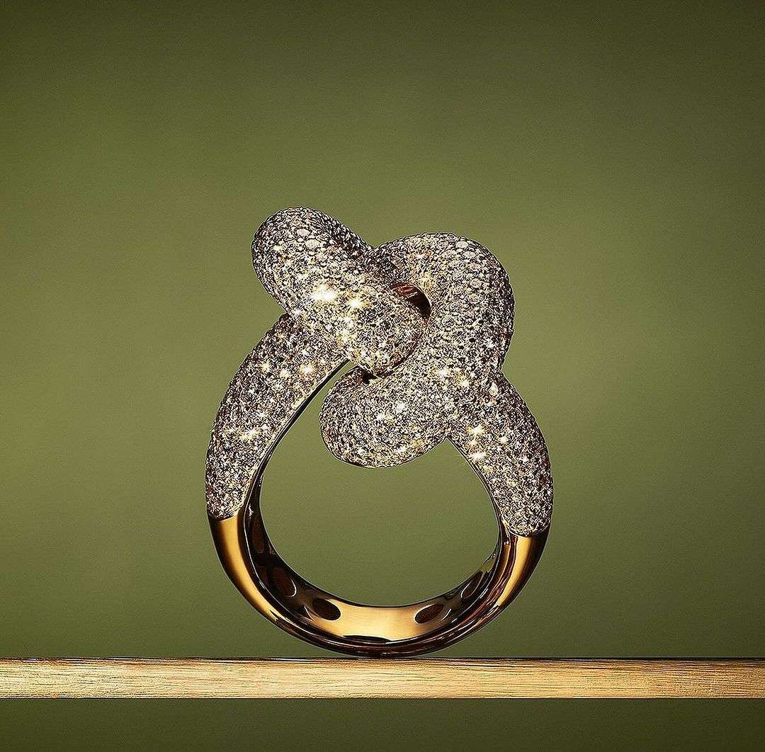 Elegant knot ring encrusted with diamonds on a wooden surface against an olive-green background, showcasing jewelry craftsmanship and design.