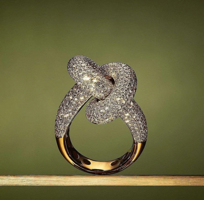 Elegant knot ring encrusted with diamonds on a wooden surface against an olive-green background, showcasing jewelry craftsmanship and design.