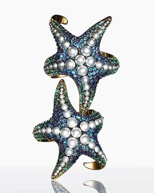 Two starfish cuff bracelets featuring pearls and gemstones, stacked on a reflective surface against a white background. Jewellery still life.