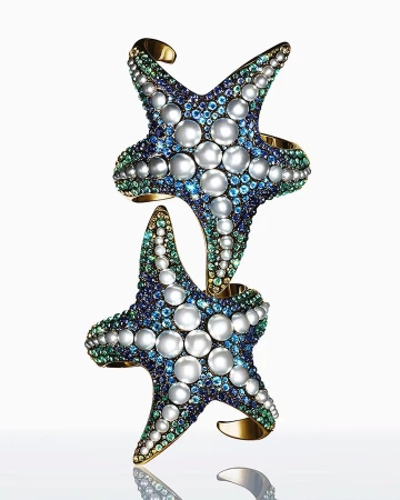 Two starfish cuff bracelets featuring pearls and gemstones, stacked on a reflective surface against a white background. Jewellery still life.