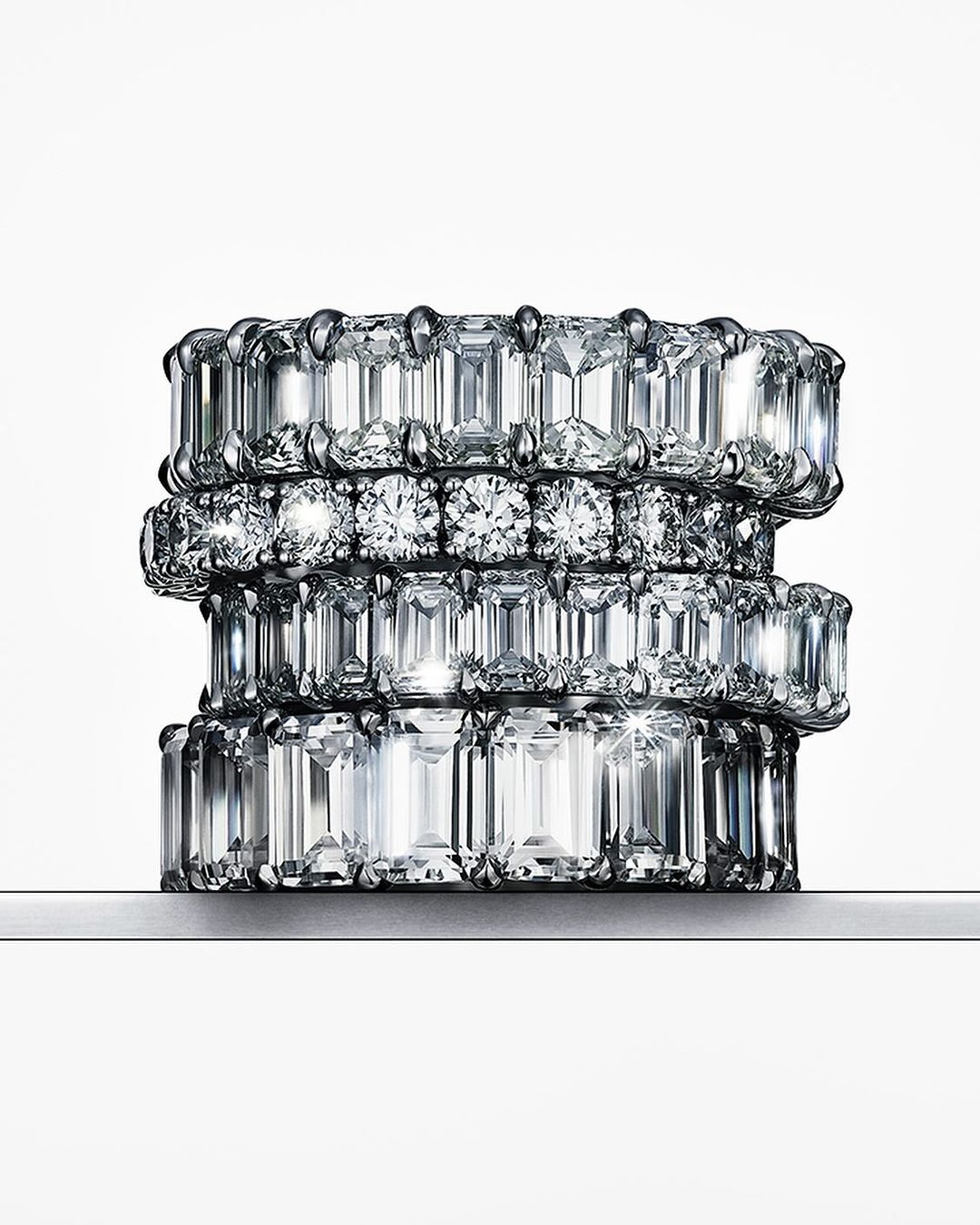 Stack of four eternity rings featuring clear diamonds in varying cuts on a white background, jewellery photography.