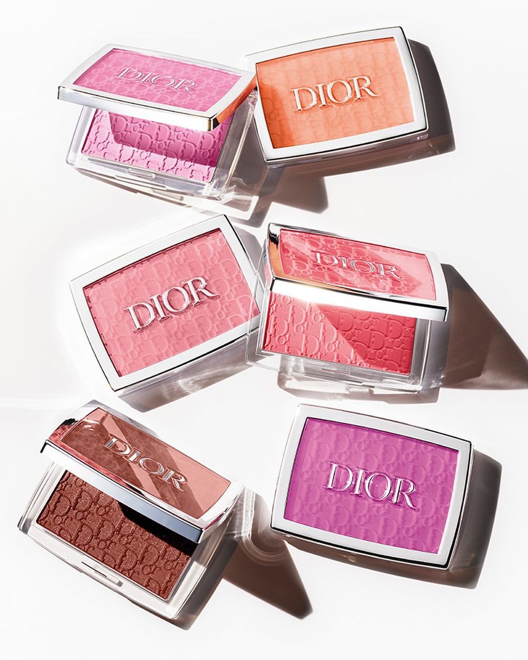 Several blush compacts from Dior in various colors are arranged on a white surface, showcasing the makeup product's packaging.