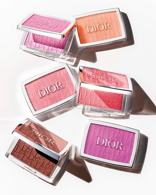 Several blush compacts from Dior in various colors are arranged on a white surface, showcasing the makeup product's packaging.