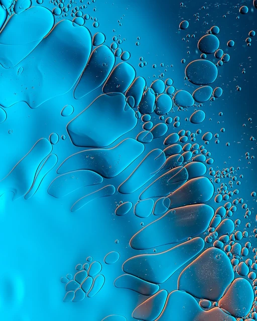 Abstract macro photograph of translucent blue and orange oil droplets floating in water, creating a textured fluid art background.