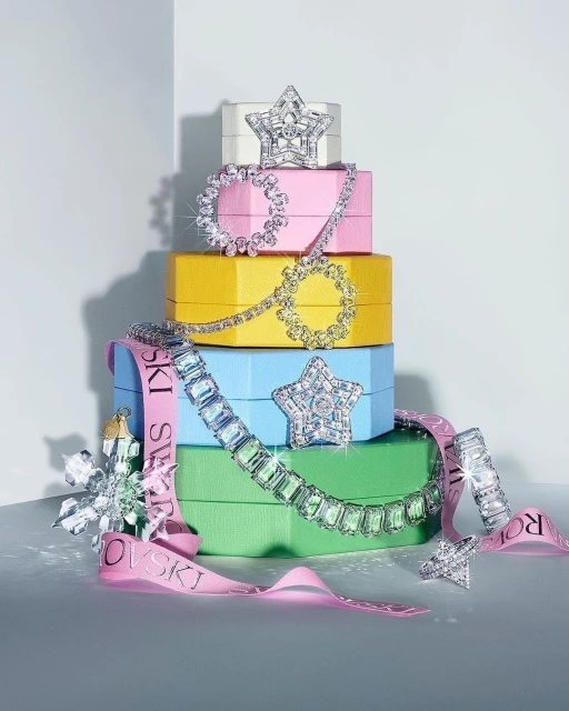 Colorful tower of jewelry boxes stacked with star and circle shaped jewel-encrusted accessories with a pink ribbon on white surface.