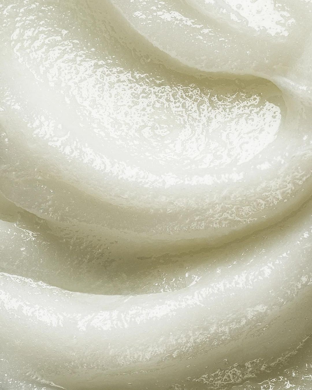 Close-up of a thick, textured, white cosmetic cream or lotion forming a swirl, highlighting its rich consistency and smooth application.