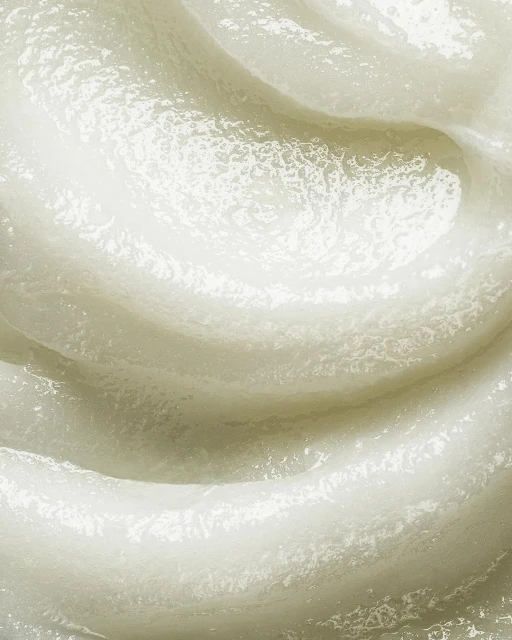 Close-up of a thick, textured, white cosmetic cream or lotion forming a swirl, highlighting its rich consistency and smooth application.