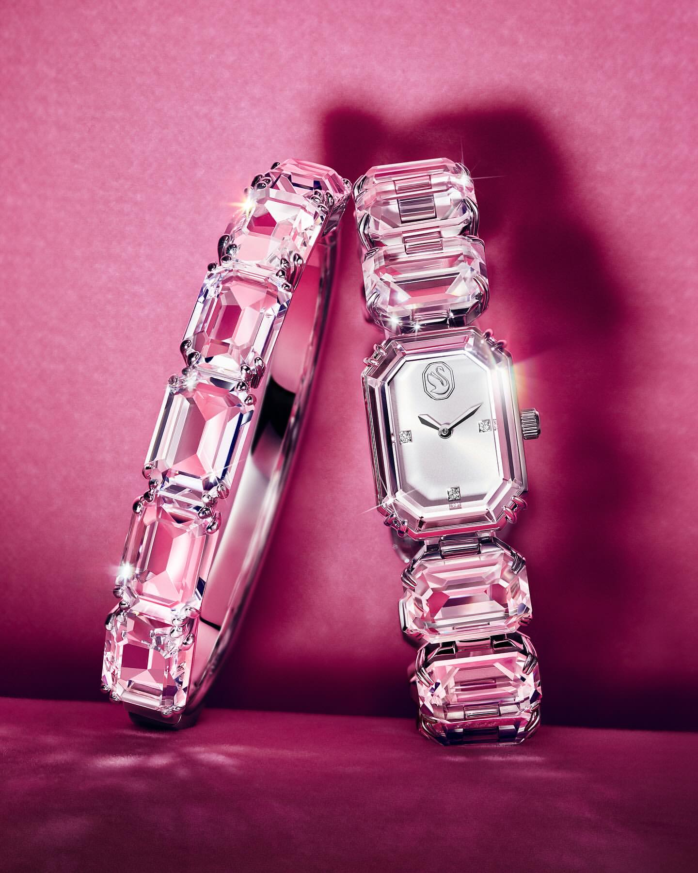 Still life studio shot of a silver-tone metal bracelet and wristwatch encrusted with pink crystal stones against a pink backdrop.
