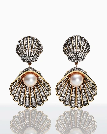 Pair of seashell-shaped dangle earrings with pearl accent and diamond embellishments, studio shot on a bright white reflective surface.