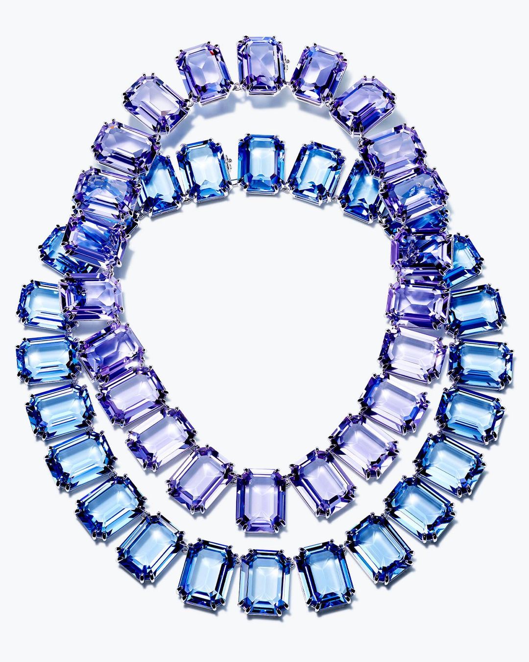 Overhead shot of a gemstone necklace with rectangular light blue and purple stones linked with silver settings on a white backdrop.