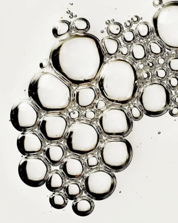 A macro photograph showcases a cluster of clear, round bubbles against a bright white background, creating a minimalist, abstract visual.