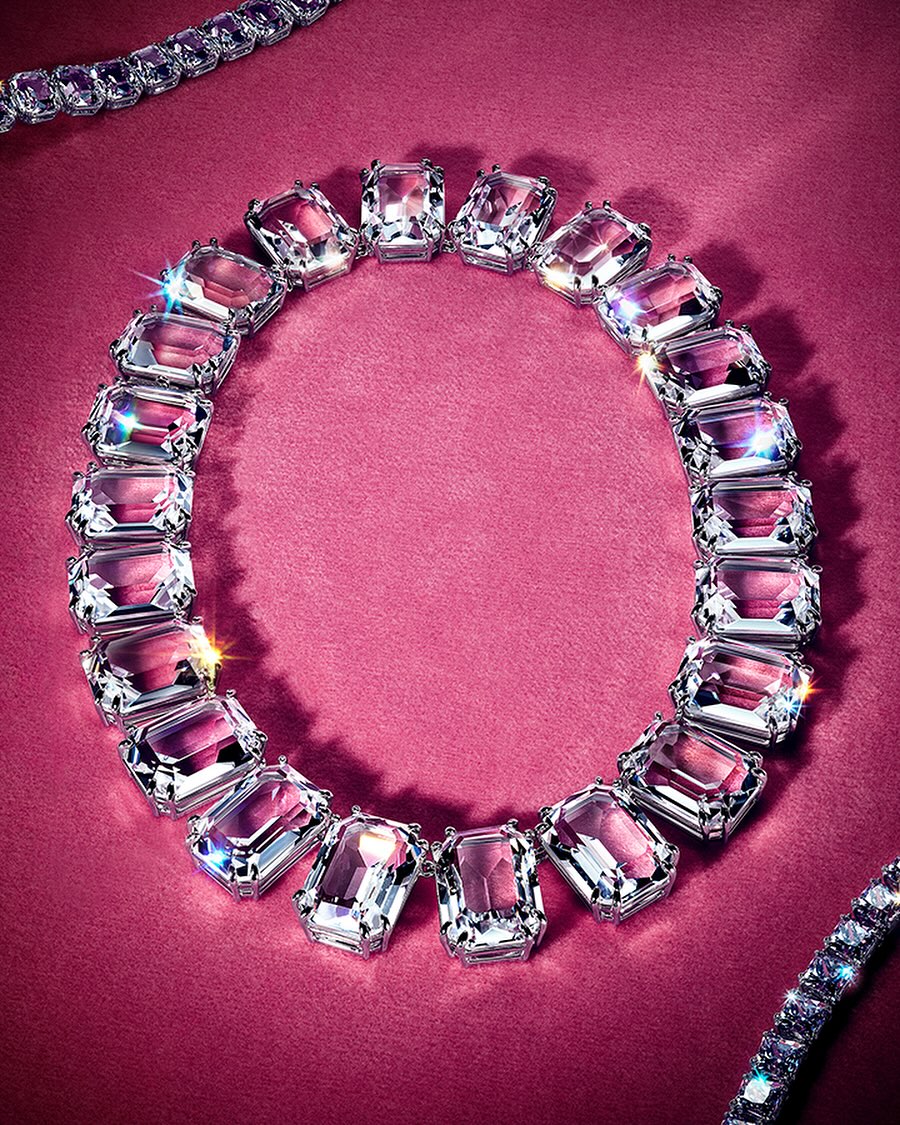 Necklace featuring large clear gemstones in silver settings on a textured magenta background with sparkling accents. Jewelry.