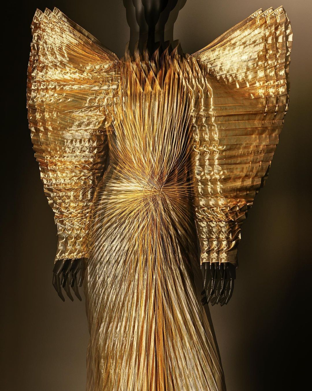 A gilded haute couture gown on a mannequin displays intricate folds and radiant metallic fabric in a studio setting, emphasizing fashion and design.