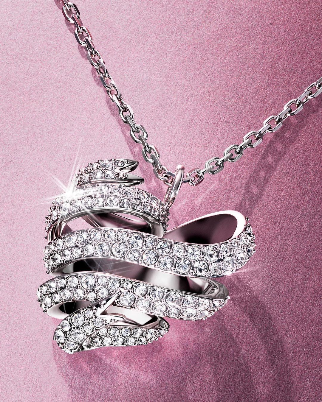 Sparkling crystal pendant necklace with a silver chain and a pink backdrop. Elegant jewelry design for fashion or special occasions.