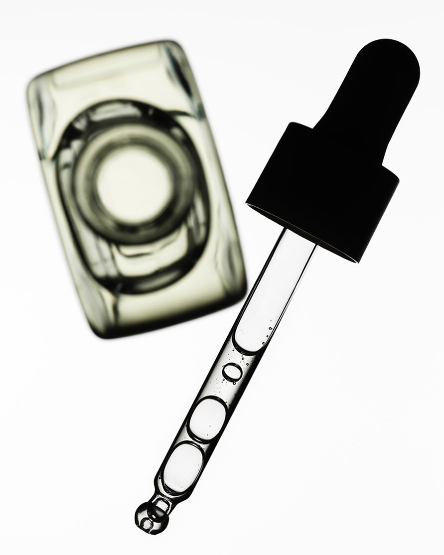 Close-up of a clear glass bottle and dropper filled with translucent liquid against a bright white background, showcasing beauty and skincare.