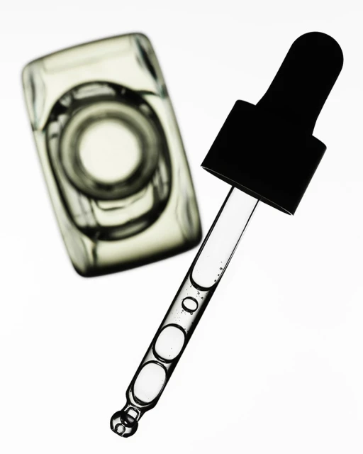 Close-up of a clear glass bottle and dropper filled with translucent liquid against a bright white background, showcasing beauty and skincare.