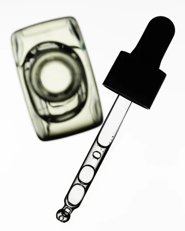 Close-up of a clear glass bottle and dropper filled with translucent liquid against a bright white background, showcasing beauty and skincare.