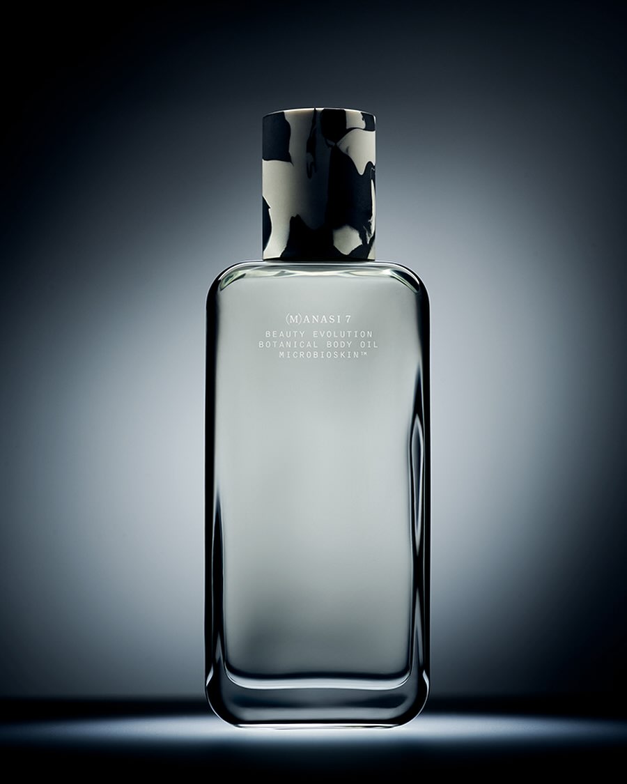Studio shot of a rectangular glass bottle with patterned black and white cap against a dark blue gradient background with studio lighting.