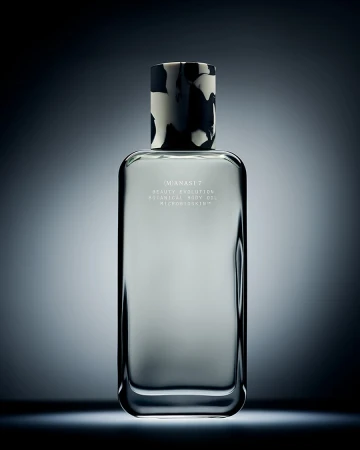 Studio shot of a rectangular glass bottle with patterned black and white cap against a dark blue gradient background with studio lighting.