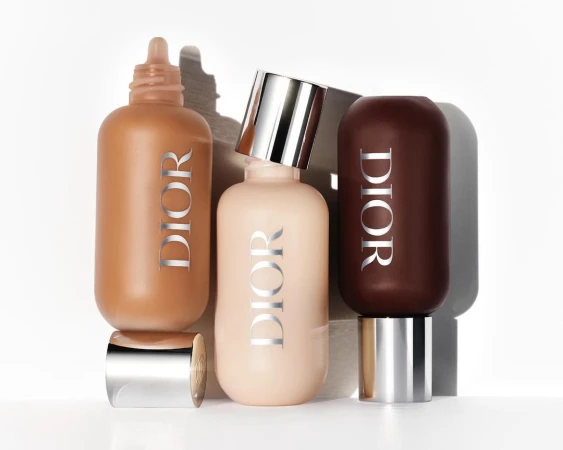 Three Dior cosmetic foundation bottles in varying shades arranged vertically against a white seamless background