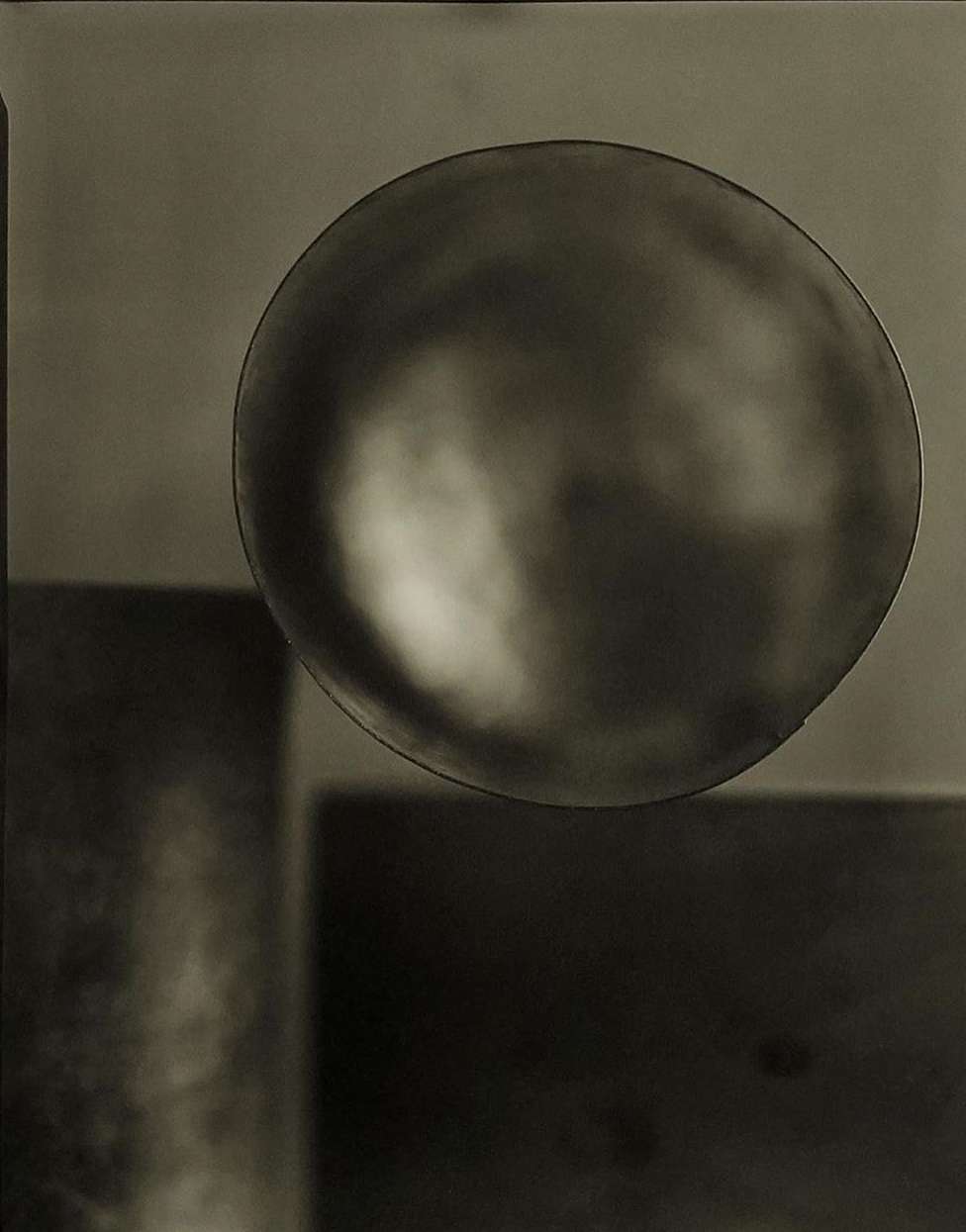 Still life photograph of a reflective sphere balancing above a square, set against a seamless gradient background in muted brown tones.