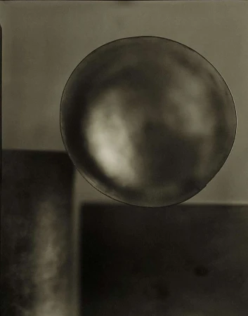 Still life photograph of a reflective sphere balancing above a square, set against a seamless gradient background in muted brown tones.