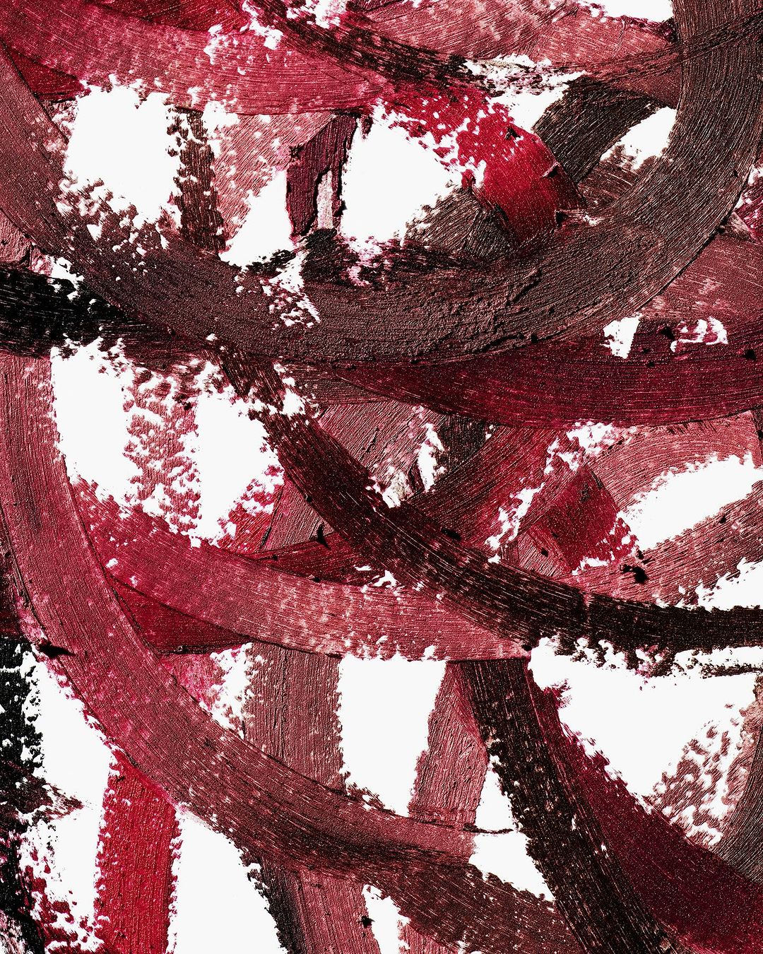 Abstract close-up of smudged, swirling burgundy and brown lipstick samples on a white background, creating a textured, artistic effect.