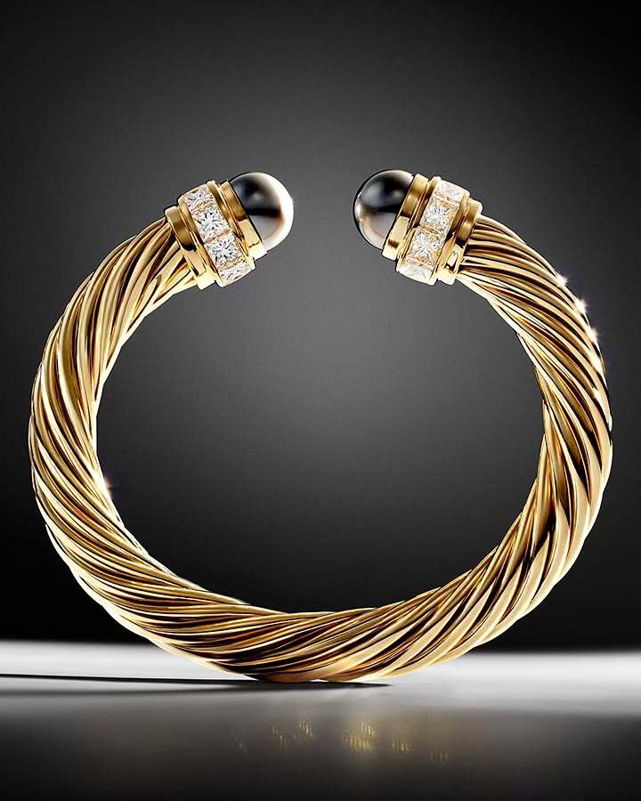 Gold-tone twisted bangle bracelet with black pearl accents and diamond embellishments, presented against a gradient gray background.