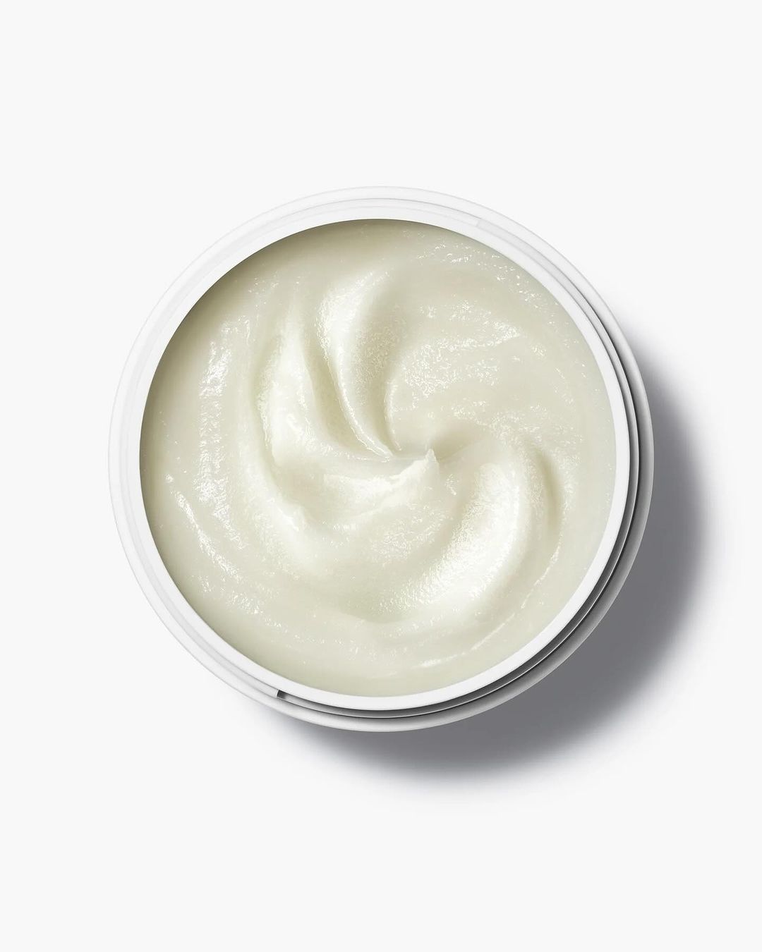 Overhead view of a white jar filled with a creamy, white substance, likely a skincare product, set against a clean, bright white background.