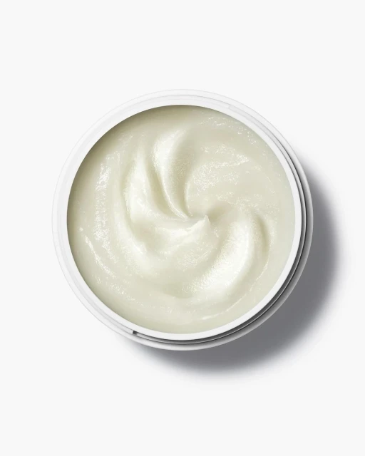 Overhead view of a white jar filled with a creamy, white substance, likely a skincare product, set against a clean, bright white background.
