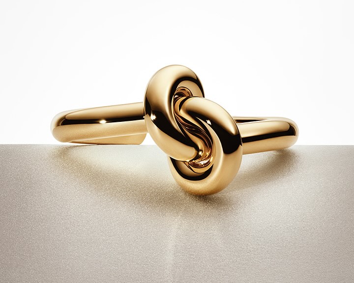 Close-up of a shiny gold knot ring on a textured surface, studio lighting, jewelry advertisement, product photography, beauty shot.