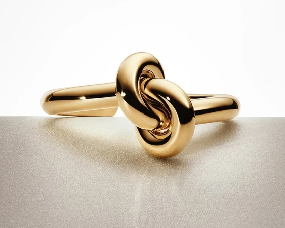 Close-up of a shiny gold knot ring on a textured surface, studio lighting, jewelry advertisement, product photography, beauty shot.
