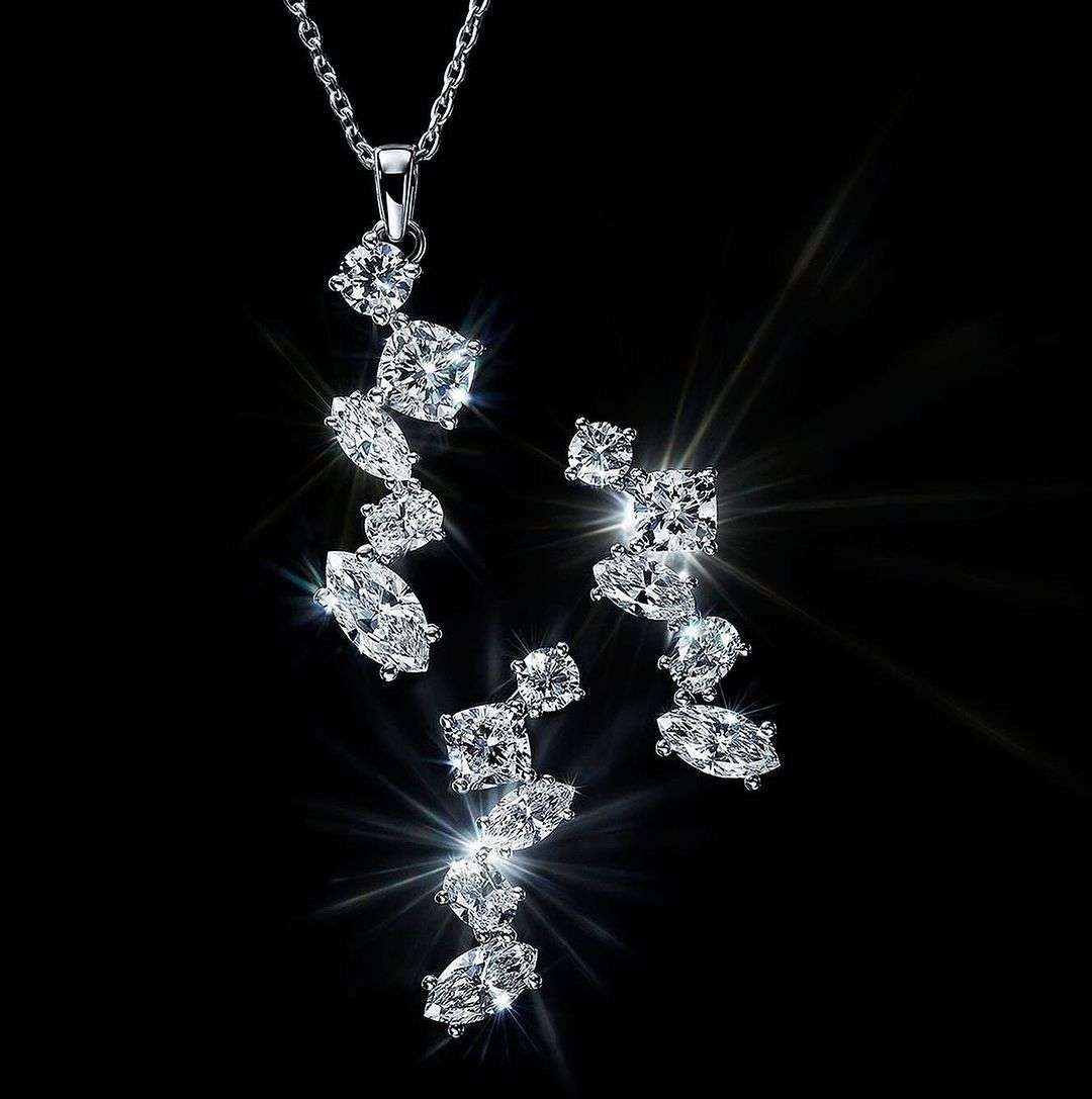 Elegant jewelry set on a black background showcasing a silver necklace and matching earrings adorned with sparkling, clear gemstones.