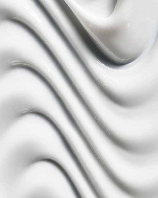 Close-up abstract texture of thick, smooth, glossy white cream or lotion with curving ridges and shadows filling the entire frame.