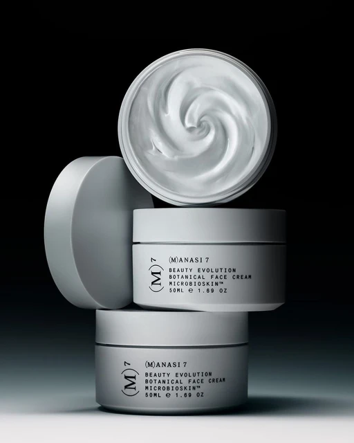 Three white cosmetic jars are stacked. The top jar's lid is off, revealing the creamy contents. A sleek, minimalist product photography.
