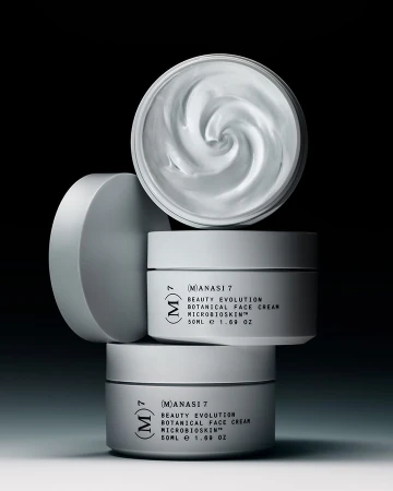 Three white cosmetic jars are stacked. The top jar's lid is off, revealing the creamy contents. A sleek, minimalist product photography.