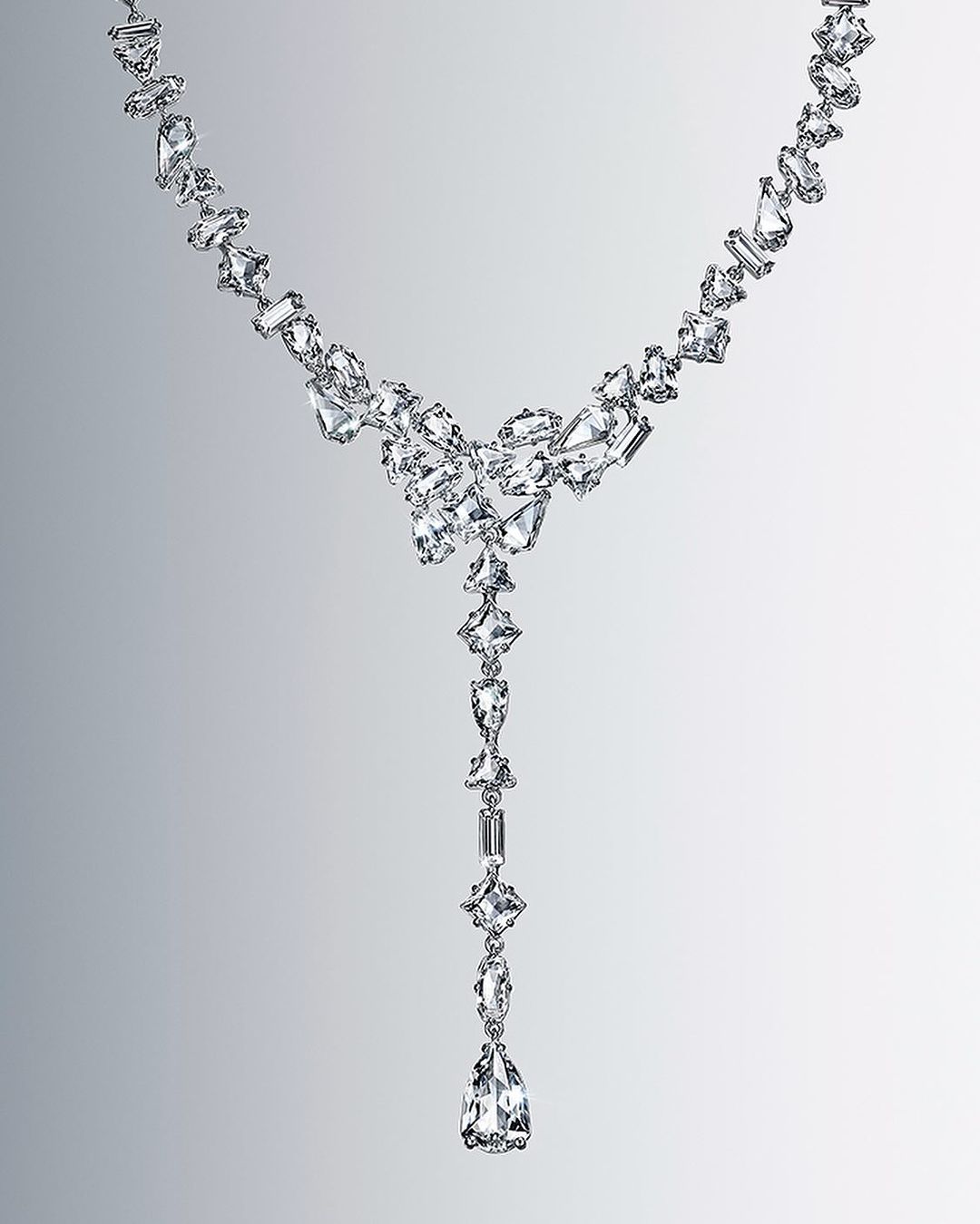 Elegant, long necklace features a graduated design with clear crystals in various geometric shapes on a gradient gray background.