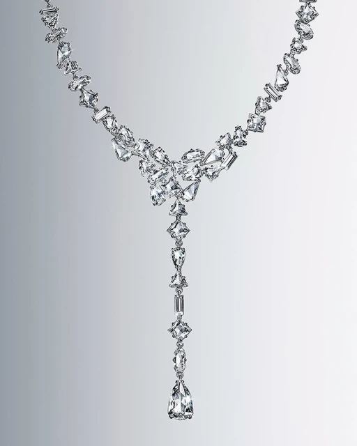 Elegant, long necklace features a graduated design with clear crystals in various geometric shapes on a gradient gray background.