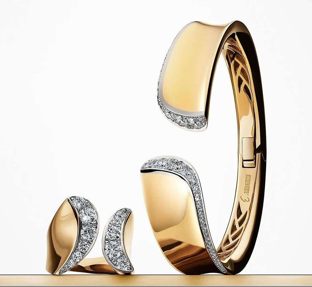 Close-up of a gold cuff bracelet and matching ring with diamond accents on a white background, showcasing jewelry design and craftsmanship.