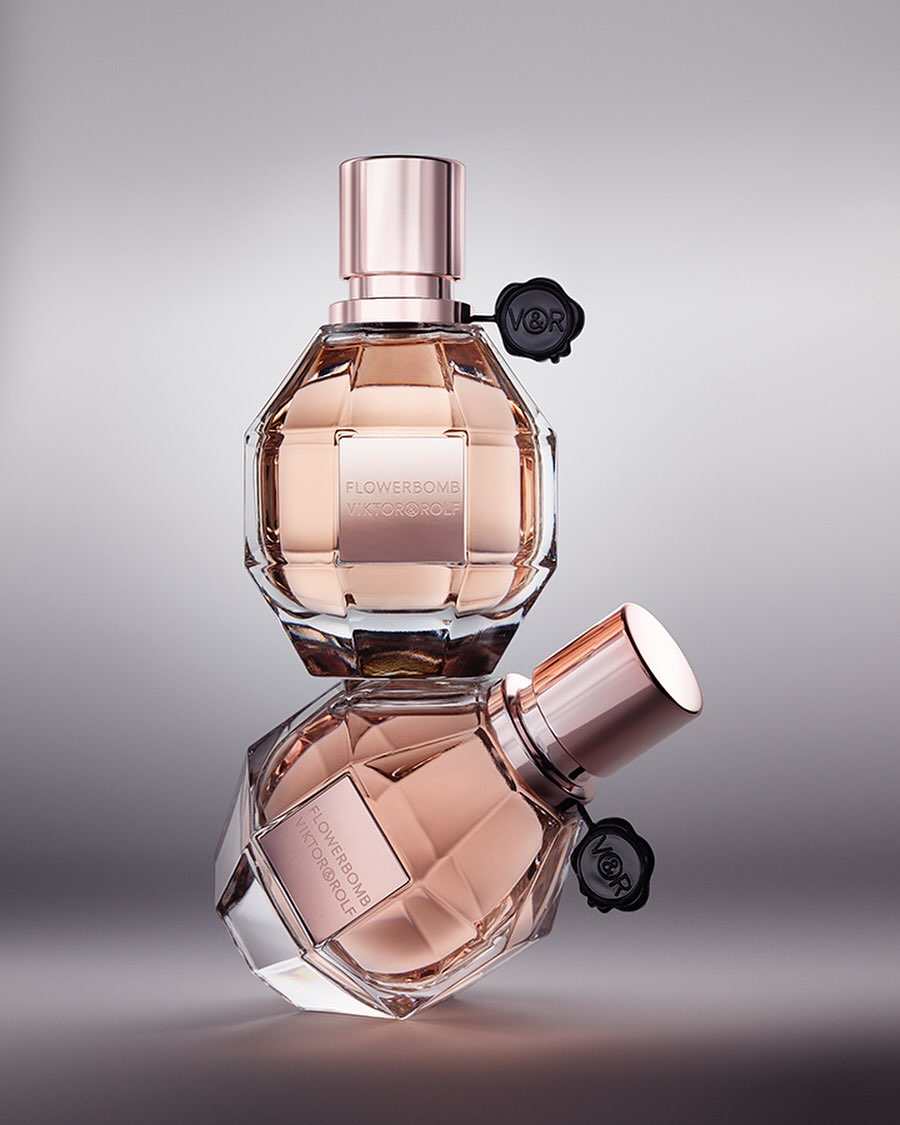 Two 'Flowerbomb' perfume bottles by Viktor & Rolf, stacked. Clear glass, rose gold accents, black logo. Luxurious and elegant beauty product.