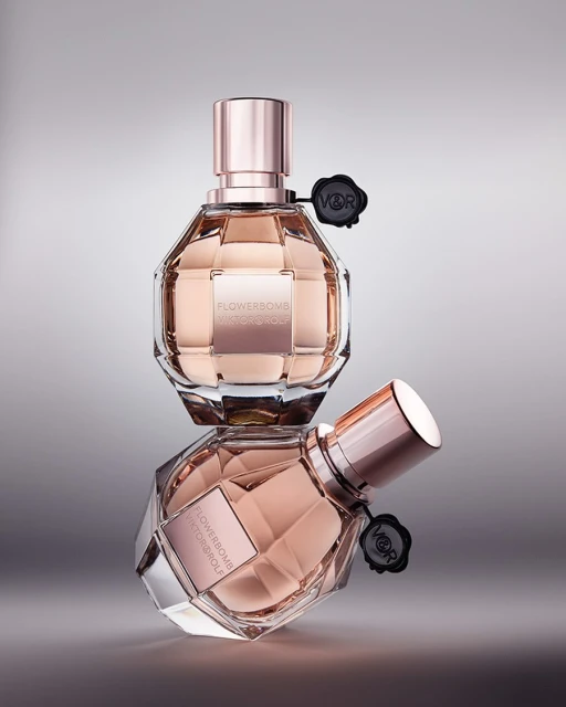 Two 'Flowerbomb' perfume bottles by Viktor & Rolf, stacked. Clear glass, rose gold accents, black logo. Luxurious and elegant beauty product.
