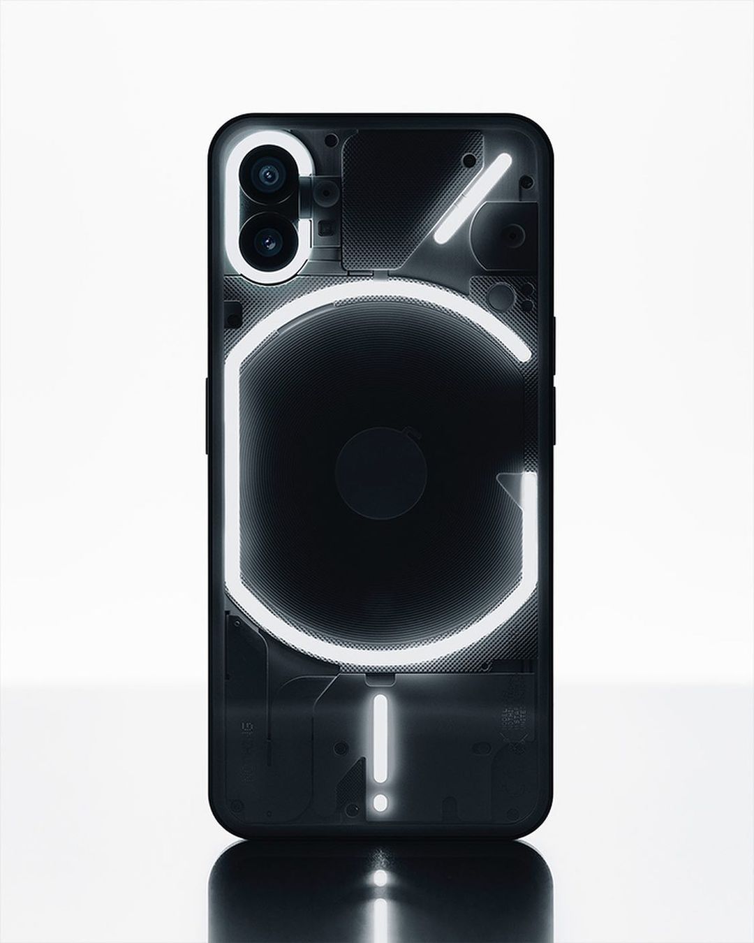 Black 'Nothing Phone' with illuminated glyph interface on a white surface. The phone features a unique transparent design and dual camera.