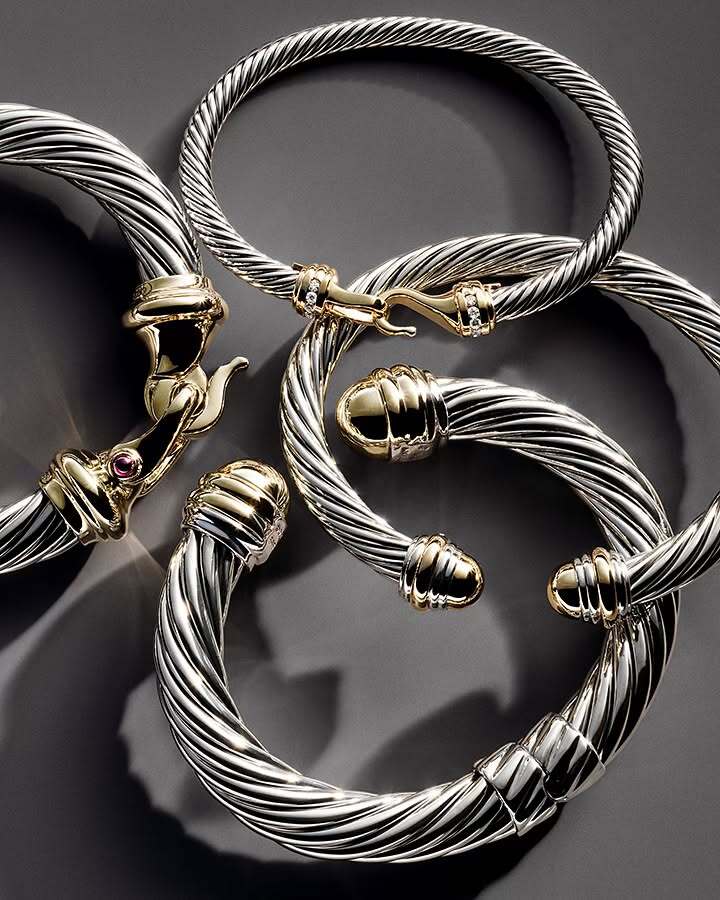 Close-up of five silver and gold cable bracelets arranged on a gray surface, showcasing their twisted designs and metallic shine.